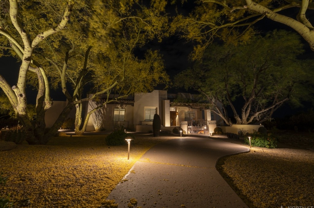 Path lights and uplit trees along a driveway to a lit home at night