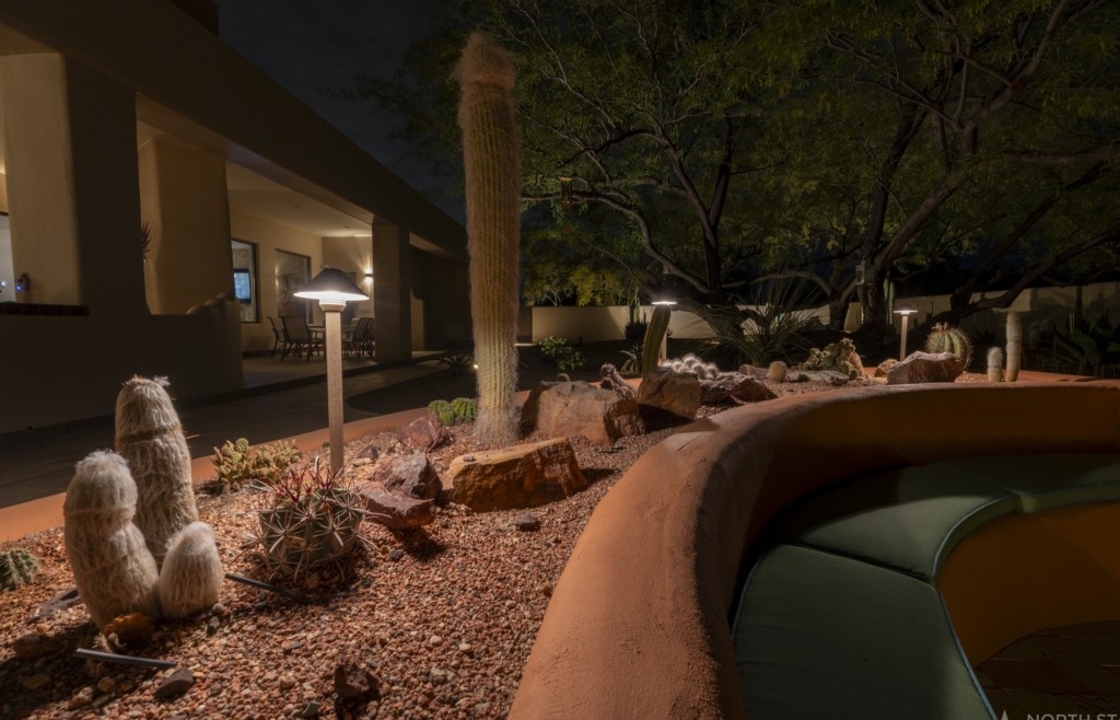 Path lights along a curved planter bed with an uplit saguaro beside a lit patio at night