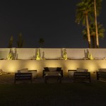 Backyard lounge seating lit at night with uplit cactus along a washed wall