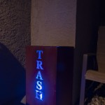 Backlit blue TRASH sign on a bin enclosure at night