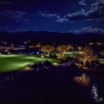 Golf course lit at night with lakes, fairway and city lights on the horizon