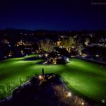 Elevated view of a lit golf course green at night with desert planting in the foreground