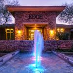 Lit stone entry of the Edge apartment community with a color-lit fountain at dusk