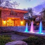 Color-lit fountain jets in front of a lit apartment leasing office at dusk