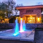 Blue and pink lit fountain jets outside the Edge community entrance at dusk