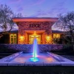 Single lit fountain jet in a reflecting pool outside a lit stone entry at dusk