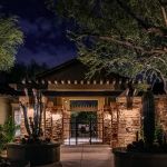 Stone entry pavilion with an iron gate lit at night, flanked by potted cactus