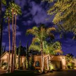 Uplit palms and a lit stucco home at night under a cloudy sky