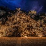 Uplit rock outcrop and desert planting beside a paver drive at night