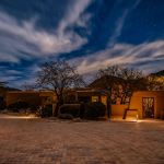 Adobe-style home and paver drive lit at night with mountains behind