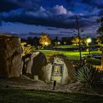 Lit boulder outcrop with a dedication plaque beside a golf course green at night