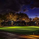 Golf green and cart path lit at night with uplit desert trees