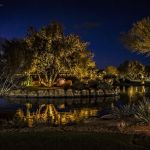 Uplit trees on a golf course island reflected in the lake at night