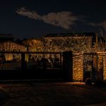 Stone entry pillars and an iron gate lit at night at a desert estate