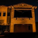 Lit two-story stucco garage elevation with a shade canopy at night