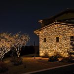 Stone garage elevation lit at night with an uplit desert tree