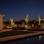 Backyard pool, lawn and patio lit at night with uplit saguaro cactus at dusk