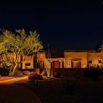 Adobe-style home lit at night with uplit desert trees and a flagstone walkway