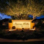Illuminated Sierra Hills entry monument sign beneath a large uplit tree at dusk