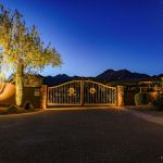 Iron community entry gate lit at dusk with an uplit tree and mountains behind