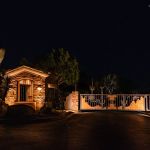 Lit gatehouse and decorative entry gate at a community entrance at night