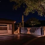 Community entry gate and call box lit at night with an uplit saguaro