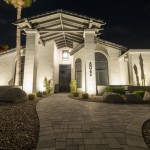 Lit entry portico and paver walkway of a white stucco home at night