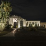 White stucco home lit at night with a lit walkway and uplit desert planting