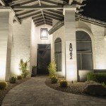 Lit entry courtyard of a white stucco home at night with a hanging lantern and uplit planting