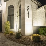 Uplit agave stalk and barrel cactus against a lit white stucco wall at night