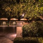 Lit walkway and entrance with a stone monument and large uplit tree at night