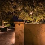 Lit stone monument marker beside a hedge at a building entrance at night