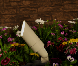 Beige bullet uplight on a spike in front of a brick wall and a bed of mixed flowers